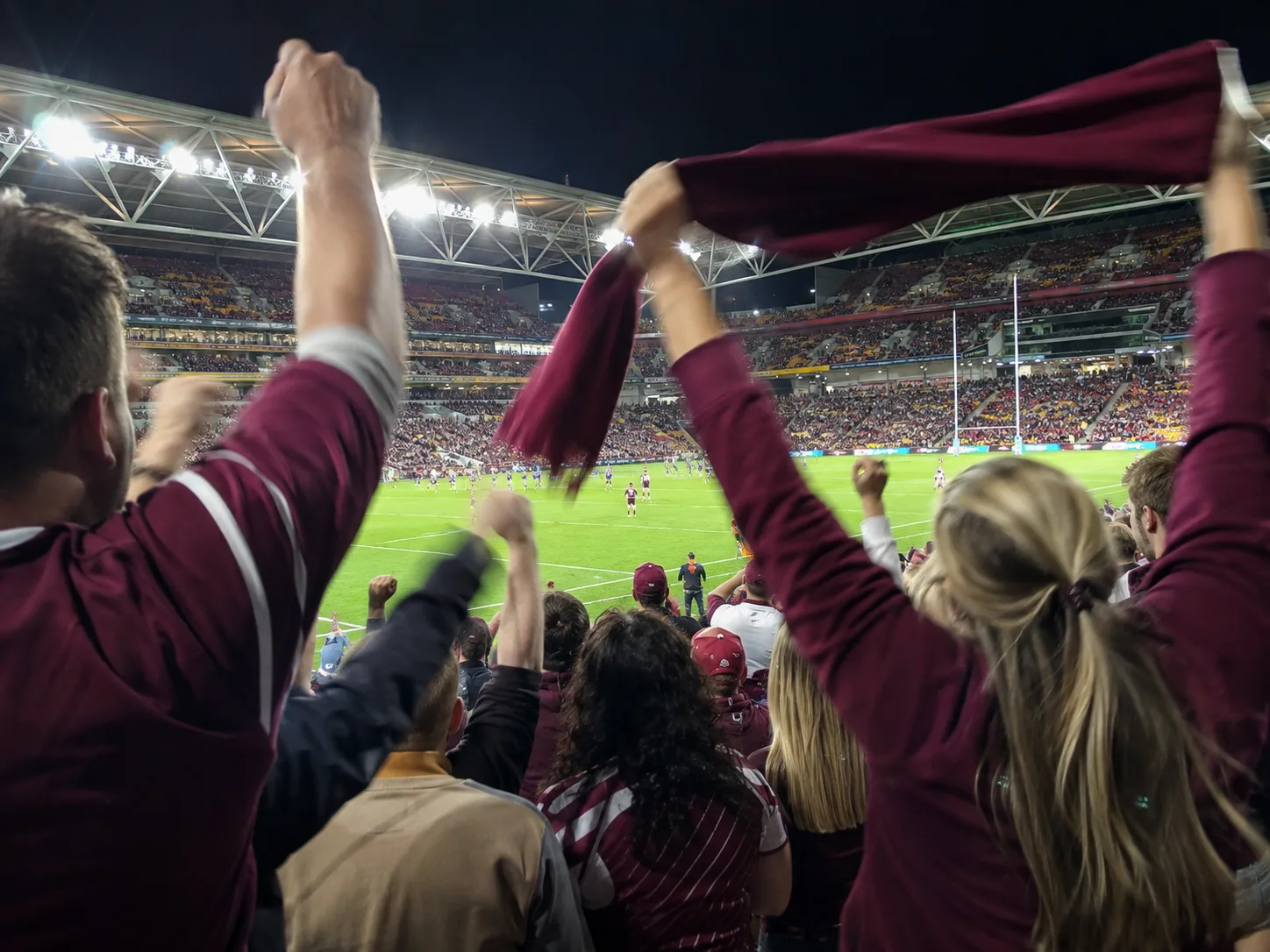 Supporters celebrating at a floodlit rugby league match